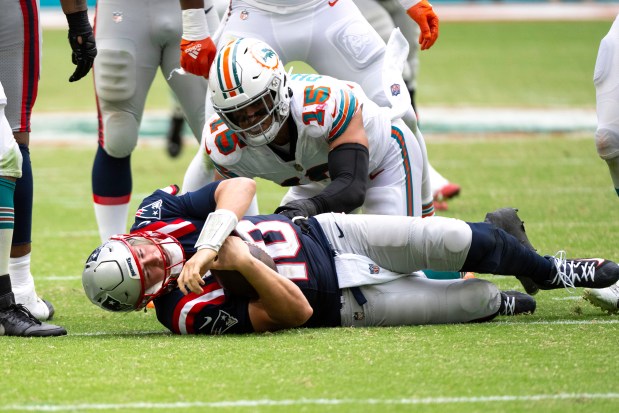 New England Patriots quarterback Mac Jones (10) lays on the field after being sacked by Miami Dolphins linebacker Jaelan Phillips (15) during an NFL football game, Sunday, Oct. 29, 2023, in Miami Gardens, Fla. (AP Photo/Doug Murray)