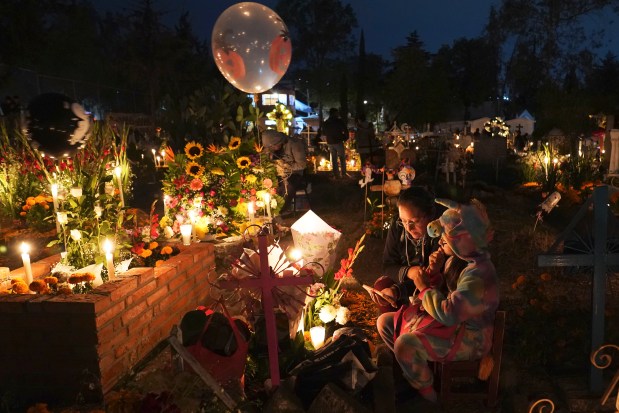 People sit around a child's tomb in the San Gregorio Atlapulco cemetery during Day of the Dead festivities on the outskirts of Mexico City, early Wednesday, Nov. 1, 2023. In a tradition that coincides with All Saints Day on Nov. 1 and All Souls Day on Nov. 2, families decorate graves with flowers and candles and spend the night in the cemetery, eating and drinking as they keep company with their dearly departed. (AP Photo/Marco Ugarte)