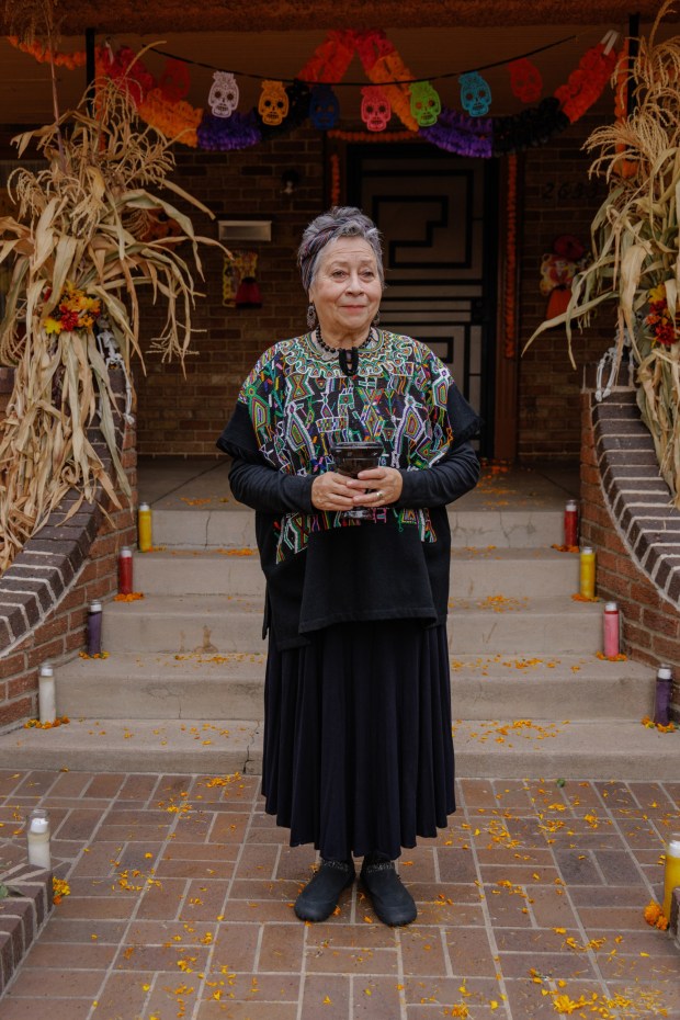 Maruca Salazar in front of her home in Denver on Oct. 26, 2023. She decorated the porch with marigold petals, candles, papel picado, and incense in honor of Dia de los Muertos. (Photo by Amanda Lopez/Special to The Denver Post)
